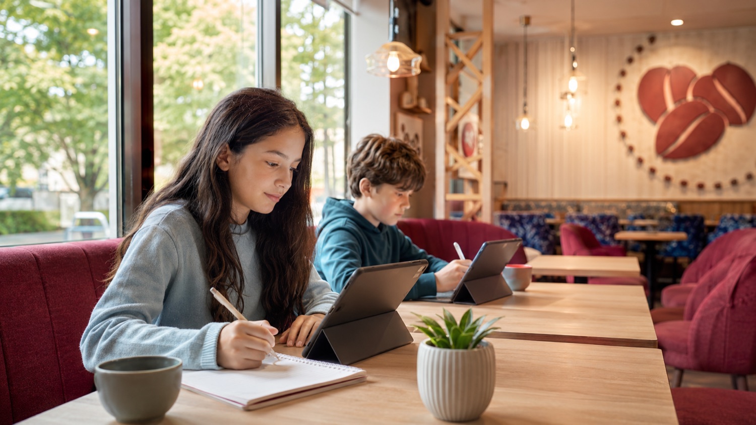 Two young learners studying individually, combining handwritten notes with digital work